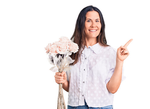 Young beautiful brunette woman holding bouquet of flowers smiling happy pointing with hand and finger to the side