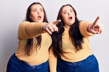 Young plus size twins wearing casual clothes pointing with finger surprised ahead, open mouth amazed expression, something on the front