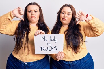 Young plus size twins holding my body my rules banner with angry face, negative sign showing dislike with thumbs down, rejection concept