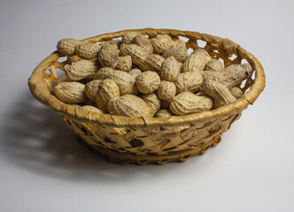 Wicker plate with peanuts in a shell on a white background