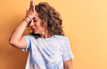 Middle age beautiful woman wearing casual dye t-shirt standing over yellow background surprised with hand on head for mistake, remember error. Forgot, bad memory concept.