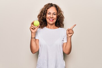 Middle age beautiful  sportswoman holding tennis ball over isolated white background smiling happy...