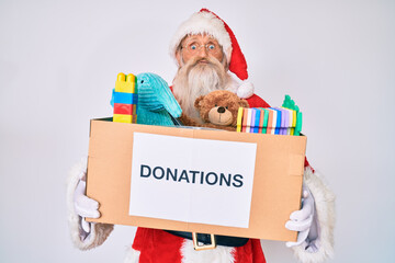 Old senior man wearing santa claus costume holding donation box puffing cheeks with funny face....