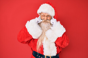 Old senior man with grey hair and long beard wearing traditional santa claus costume covering ears with fingers with annoyed expression for the noise of loud music. deaf concept.