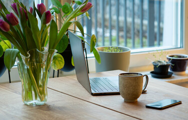 Modern home office during spring time. Laptop, mobile phone, coffee cup and fresh tulips in a vase...