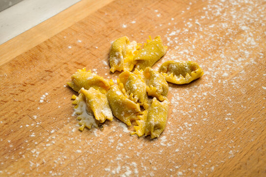Ravioli del plin, typical pasta from Langhe, Piedmont, Italy - freshly made raw agnolotti on wooden cutting board