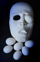 A white scary theater mask lies next to the chicken eggs