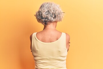 Senior grey-haired woman wearing casual clothes standing backwards looking away with crossed arms