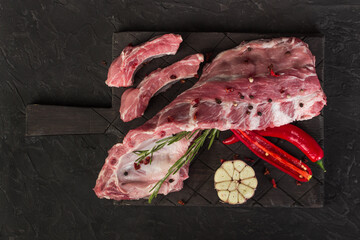 Raw pork ribs on a dark board with rosemary, hot pepper and a chock