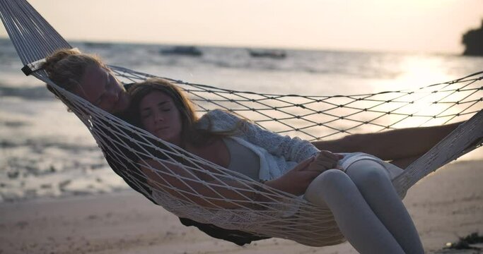Young happy couple waking up in the morning in tropical hammock. Playful caucasian man and woman  lying on lovely fabric sling talking and kissing. Concept of Valentine love and happiness. Slow Motion