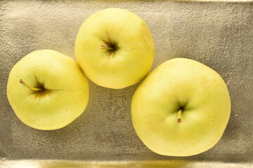 Three delicious yellow apples on a metal tray, close-up.