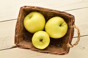 Three delicious yellow apples in a basket of vines, close-up, on a wooden table.