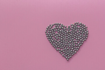 silver pearl sprinkles arranged in a heart shape on a pink rustic background. Valentine's Day, greeting card. Sprinklers for confectionery and pastry, Copy space, top view