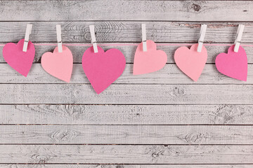 Valentine's day composition with pink paper hearts hanging from line with pegs on wooden background with empy copy space