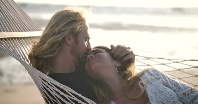 Young happy couple waking up in the morning in tropical hammock. Playful caucasian man and woman  lying on lovely fabric sling talking and kissing. Concept of Valentine love and happiness. Slow Motion