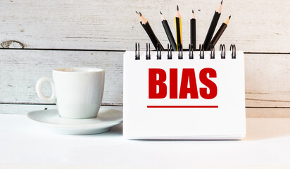 The word BIAS is written in a white notepad near a white cup of coffee on a light background