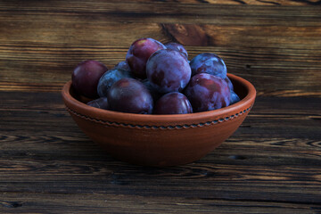 The ripe plums in a clay bowl