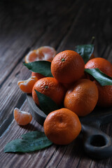 Many tangerines with green leaves lie on a wooden board, on a wooden table. Photo in a dark key