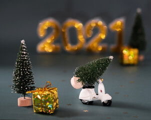 New Year's card. A miniature doll scooter with an artificial little Christmas tree on the seat. Small Christmas trees with a gift in a gold package. Figures for 2021.
