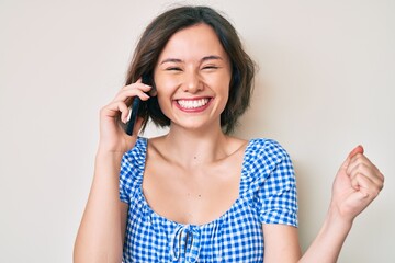 Young beautiful girl having conversation talking on the smartphone screaming proud, celebrating victory and success very excited with raised arm