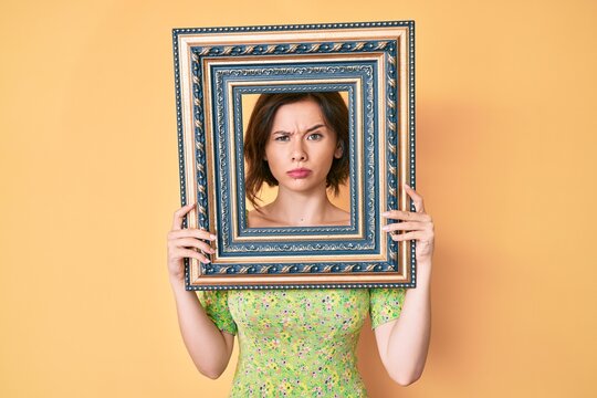 Young beautiful woman holding empty frame skeptic and nervous, frowning upset because of problem. negative person.