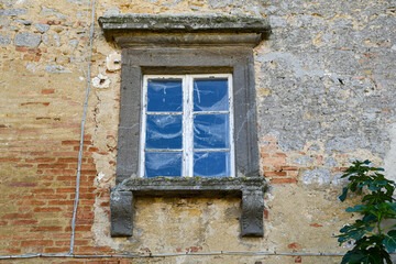 The stone framed window of an old stone and brick house with a branch of a fig tree, Volterra, Pisa, Tuscany, Italy