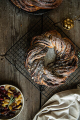 Homemade yeast dough wreath (Kranz, couronne, brioche ) with chocolate and dried fruits filling dusted with sugar powder on cooling rack on wooden table.