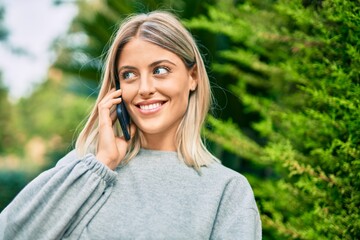 Young blonde girl smiling happy talking on the smartphone at the park