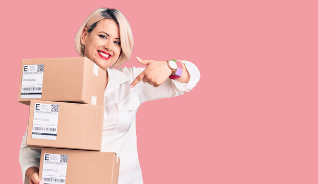 Young blonde plus size woman holding delivery cardboard package smiling happy pointing with hand and finger