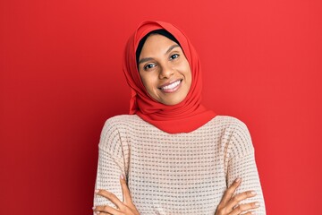 Young african american woman wearing traditional islamic hijab scarf happy face smiling with crossed arms looking at the camera. positive person.