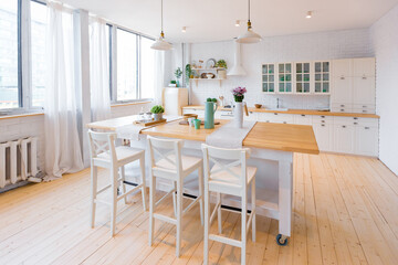 Stylish kitchen in light colors in a trendy modern duplex apartment with large high windows.