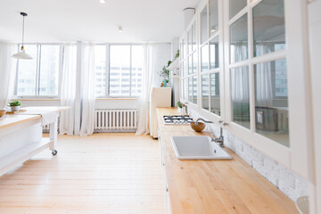 Stylish kitchen in light colors in a trendy modern duplex apartment with large high windows.