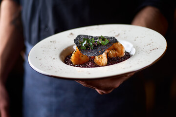 Black rice risotto. Shrimp risotto on a white plate on the table, serving in a restaurant, menu food concept