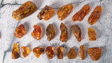 A set of different shapes and sizes of natural old yellow, orange and green Baltic amber stones on a gray plastered background.  Material for jewelers, top from above close up.