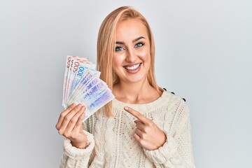 Beautiful caucasian woman holding swedish krona banknotes smiling happy pointing with hand and finger