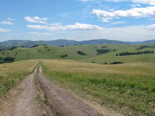 Fototapeta na wymiar Dirt road stretching into the distance beyond the horizon. The road among the green hills. Summer.