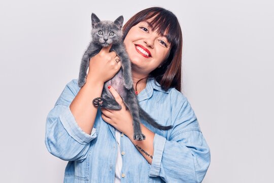 Young beautiful plus size woman smilling happy and confident. Standing with smile on face holding adorable cat over isolated white background