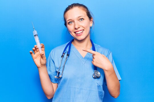 Young blonde woman wearing doctor uniform holding syringe smiling happy pointing with hand and finger
