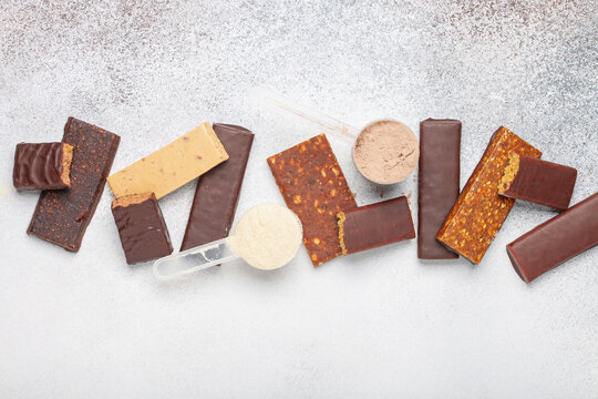 Whey protein powder in measuring scoop and different energy protein bar on grey background. Top view