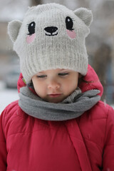 Little girl in the street in winter in a funny hat and red jacket