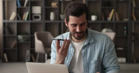 Male office employee sit at desk with laptop talk to colleague on phone speakerphone. Businessman solve business remotely by smartphone, leave voice message, share information use modern tech concept - Powered by Adobe