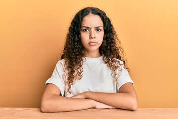 Teenager hispanic girl wearing casual clothes sitting on the table skeptic and nervous, frowning...