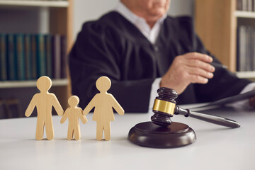 Gavel, sound block and small wooden figurines of husband, wife and kid on judge's table in courthouse during court hearing. Family law, divorce lawyer, joint custody of child and alimony concept - obrazy, fototapety, plakaty