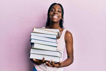 Young african american woman holding books smiling with a happy and cool smile on face. showing teeth.