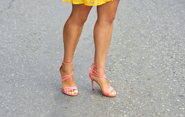 Summer legs of a young girl with a beautiful tan in sandals with heels, close-up.
