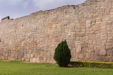 Hampi, Karnataka, India - November 5, 2013: Zanana Enclosure. Tall no-cement historic wall around the premises under light blue sky and green foliage in front