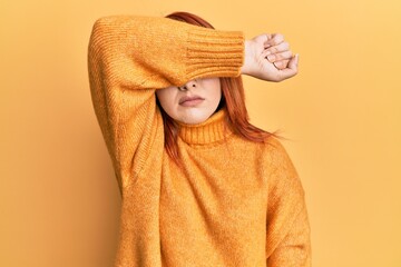 Beautiful redhead woman wearing casual winter sweater over yellow background covering eyes with arm, looking serious and sad. sightless, hiding and rejection concept