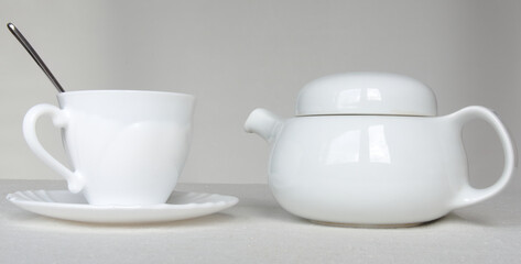 White teapot and cup on a saucer and a silver spoon