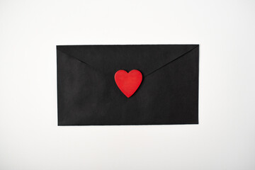 The black envelope with the red heart on the white background. Flat lay, top view. Romantic love letter for Valentine's day concept.