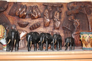 Wooden figures of elephants stand against the background of a wooden panel made by an African artist